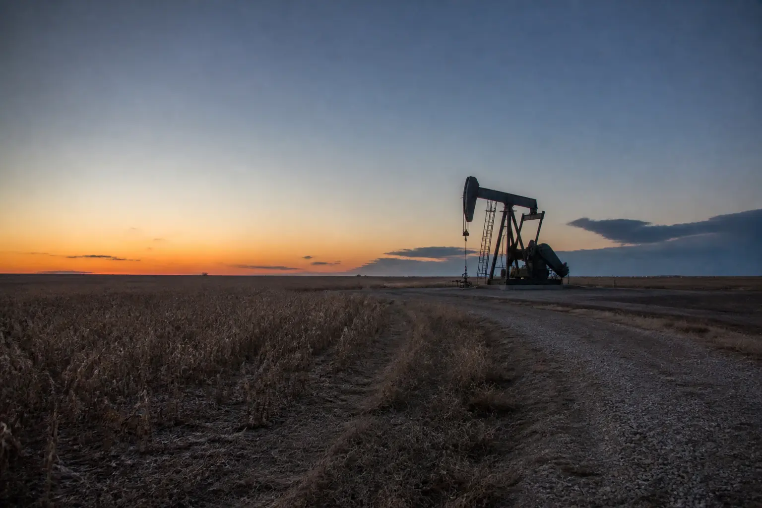 An oil pumpjack in silhouette on flat Alberta farmland at dusk