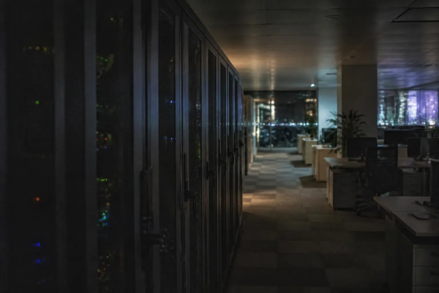 Un couloir de bureau vide et faiblement éclairé, avec des baies de serveurs, la nuit