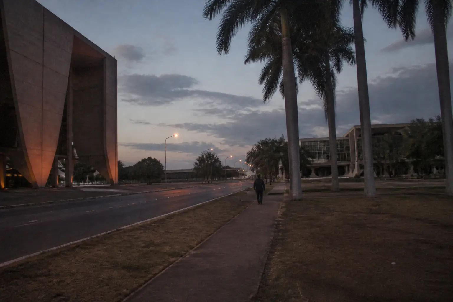 Un boulevard moderniste de l'administration à Brasília au crépuscule, bordé de palmiers et de passants au loin