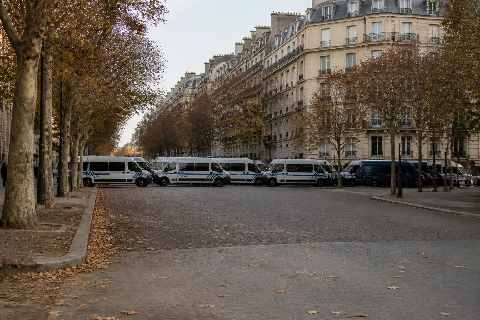 Eine abgesperrte Stadtallee in Paris, gesäumt von geparkten Polizeifahrzeugen und Steinhäusern