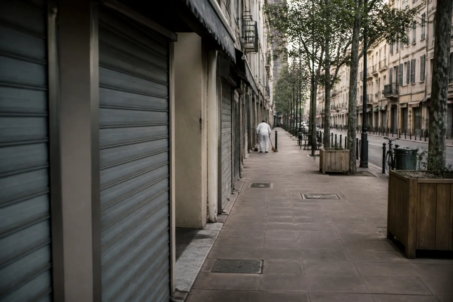 Shutters down over small shops on a quiet commercial street in a French city at dawn.