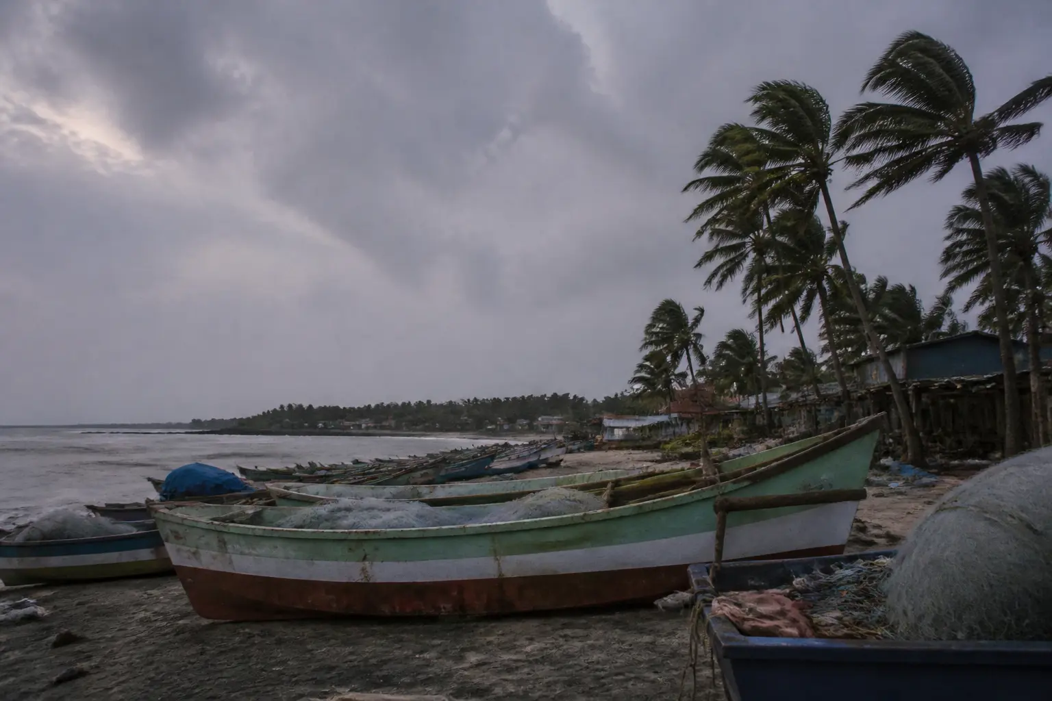 Fishing boats pulled ashore on a grey beach on India's eastern coast under an overcast sky