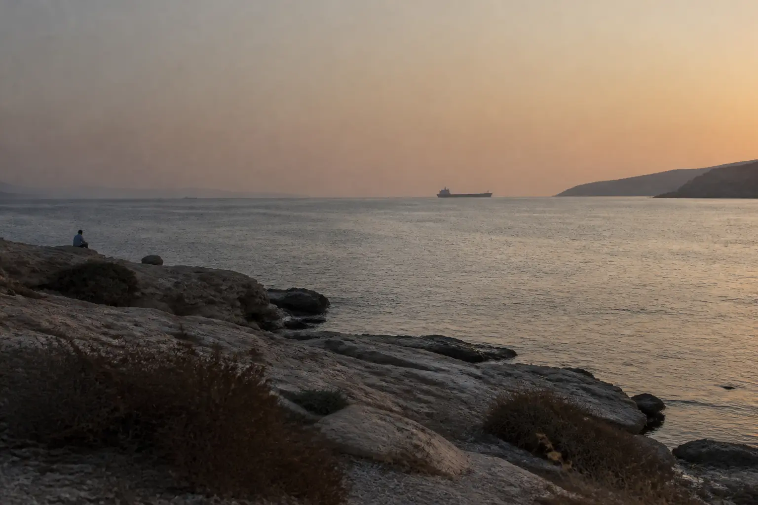 Ein Tanker im Gegenlicht am Horizont einer schmalen Golfstraße in der Abenddämmerung
