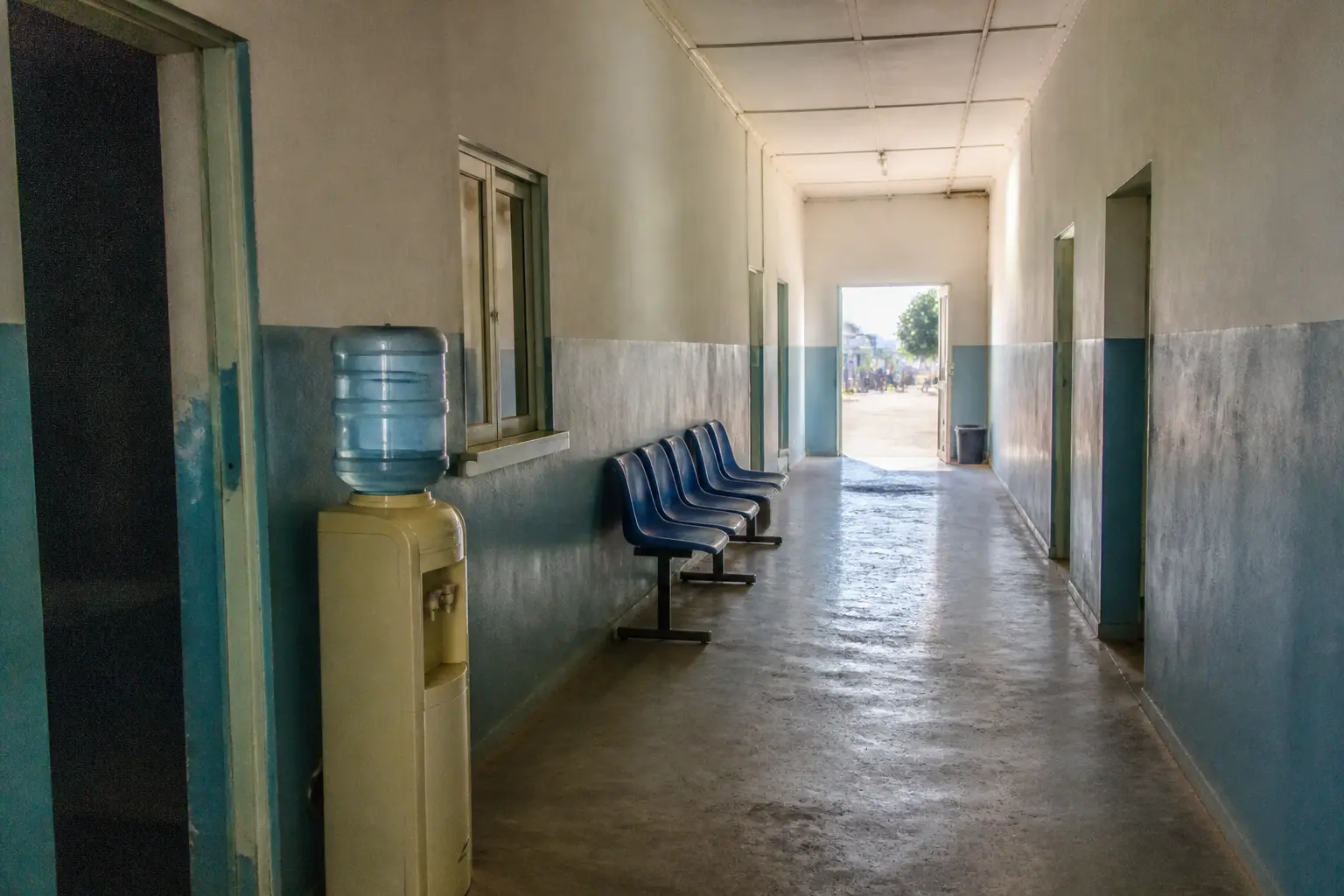 An empty hospital corridor with plastic chairs and daylight at the far end