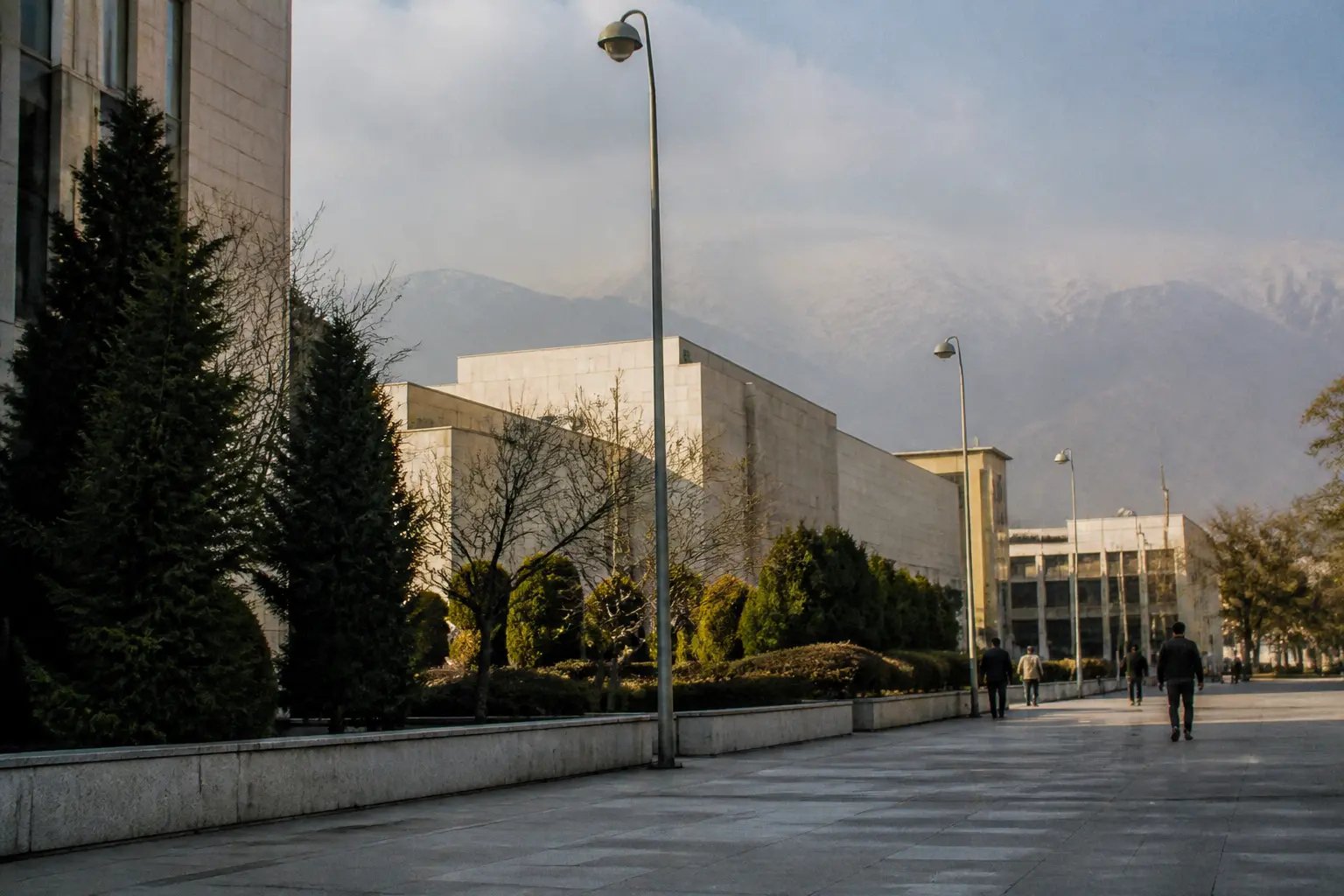 A quiet government quarter in Tehran with low buildings, trees and mountains in the distance.