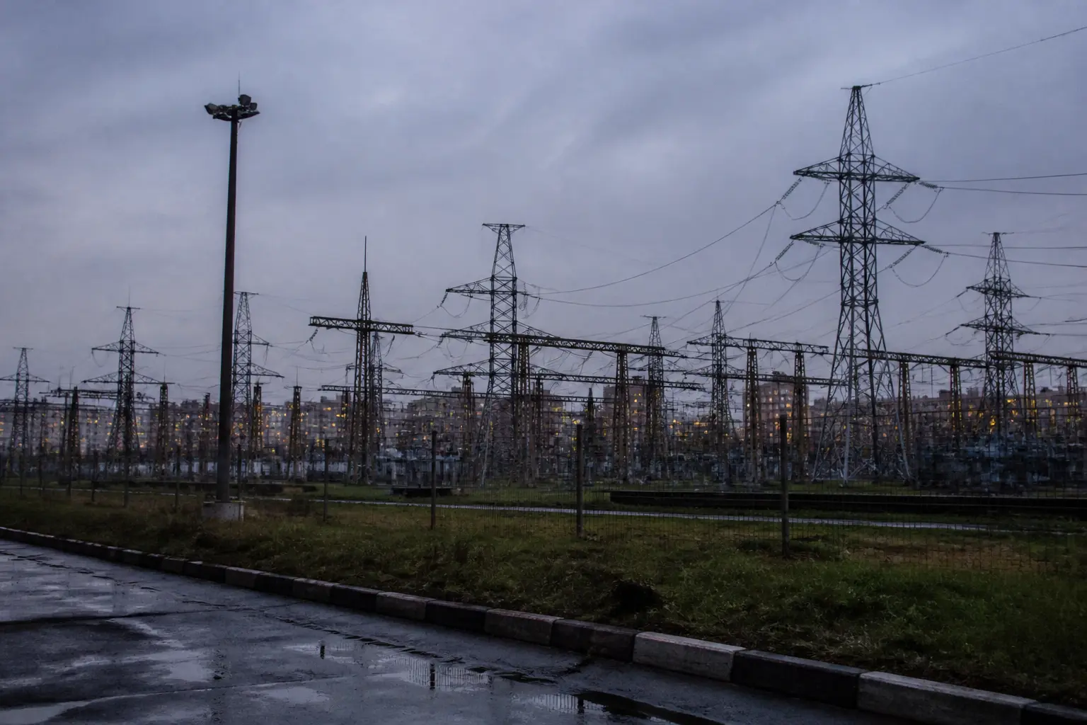 An electricity substation with pylons and transformers under a grey autumn sky at dusk.