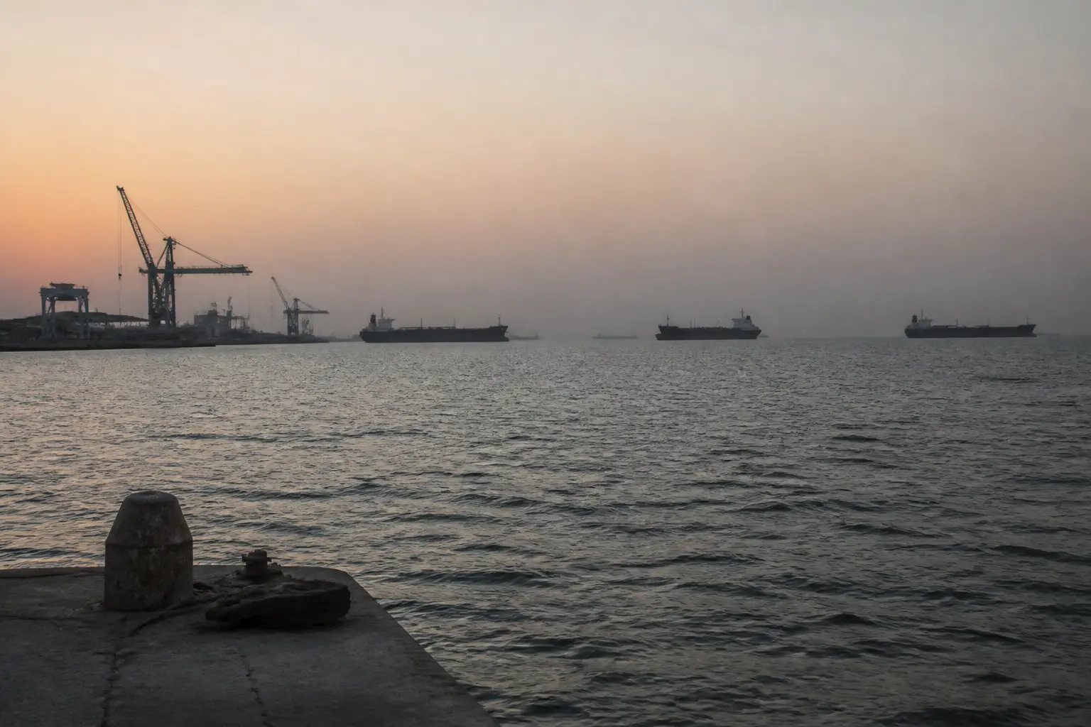 Cargo ships and cranes at a harbour on the Persian Gulf coast at dusk.